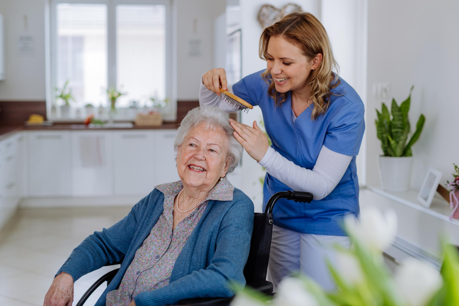 Betreuungskraft kämmt einer Seniorin liebevoll das Haar